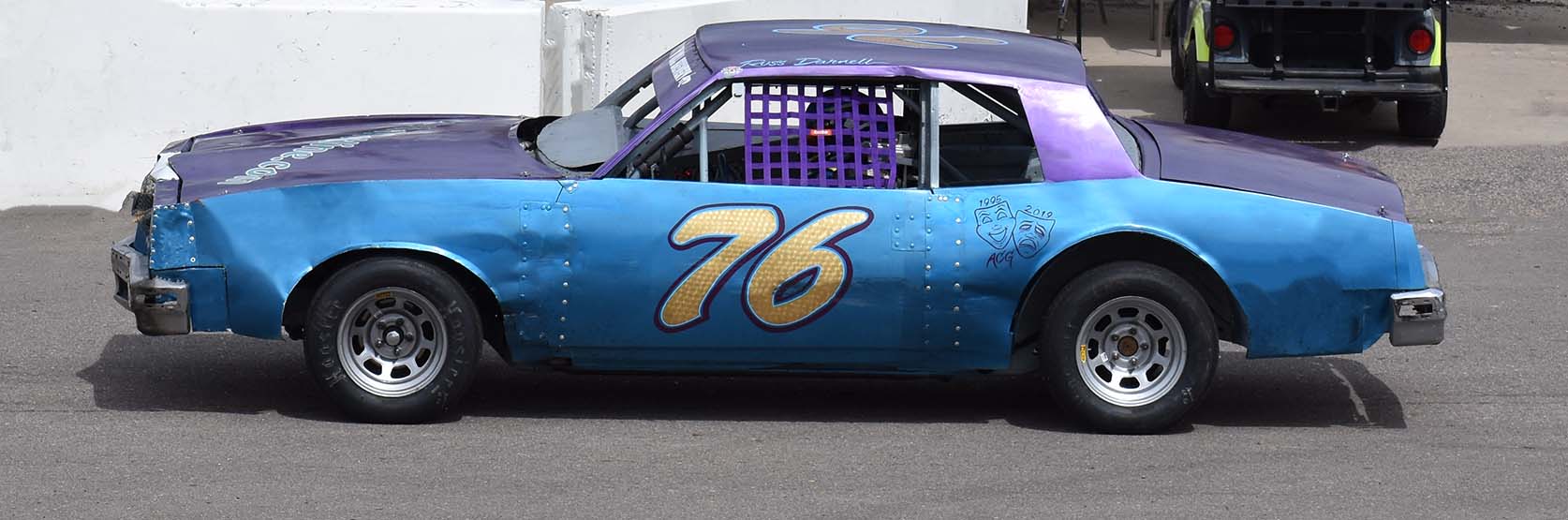 A blue and purple stock car with 76 on the door.