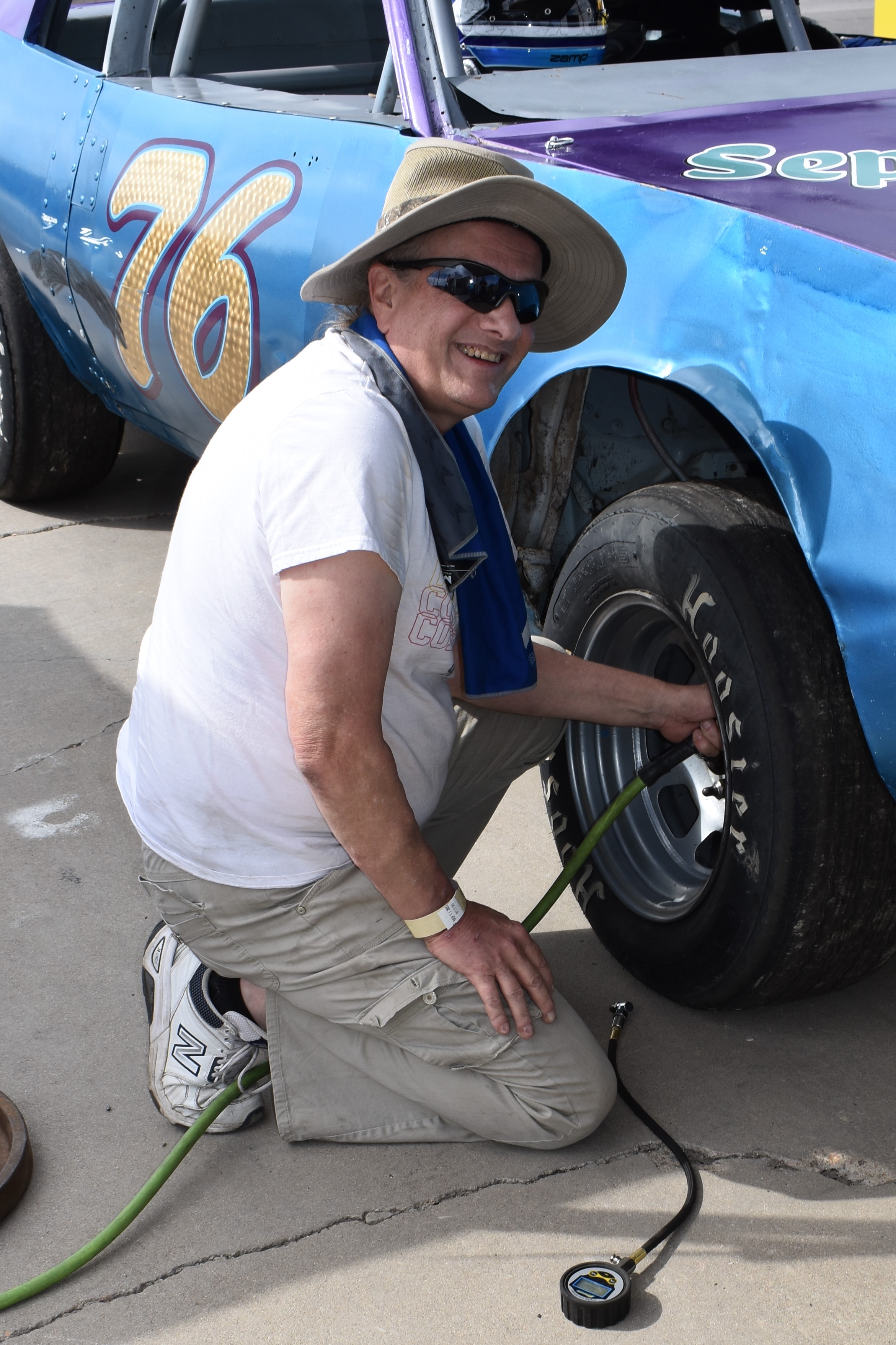 A man kneeling at the tire of a racecar.