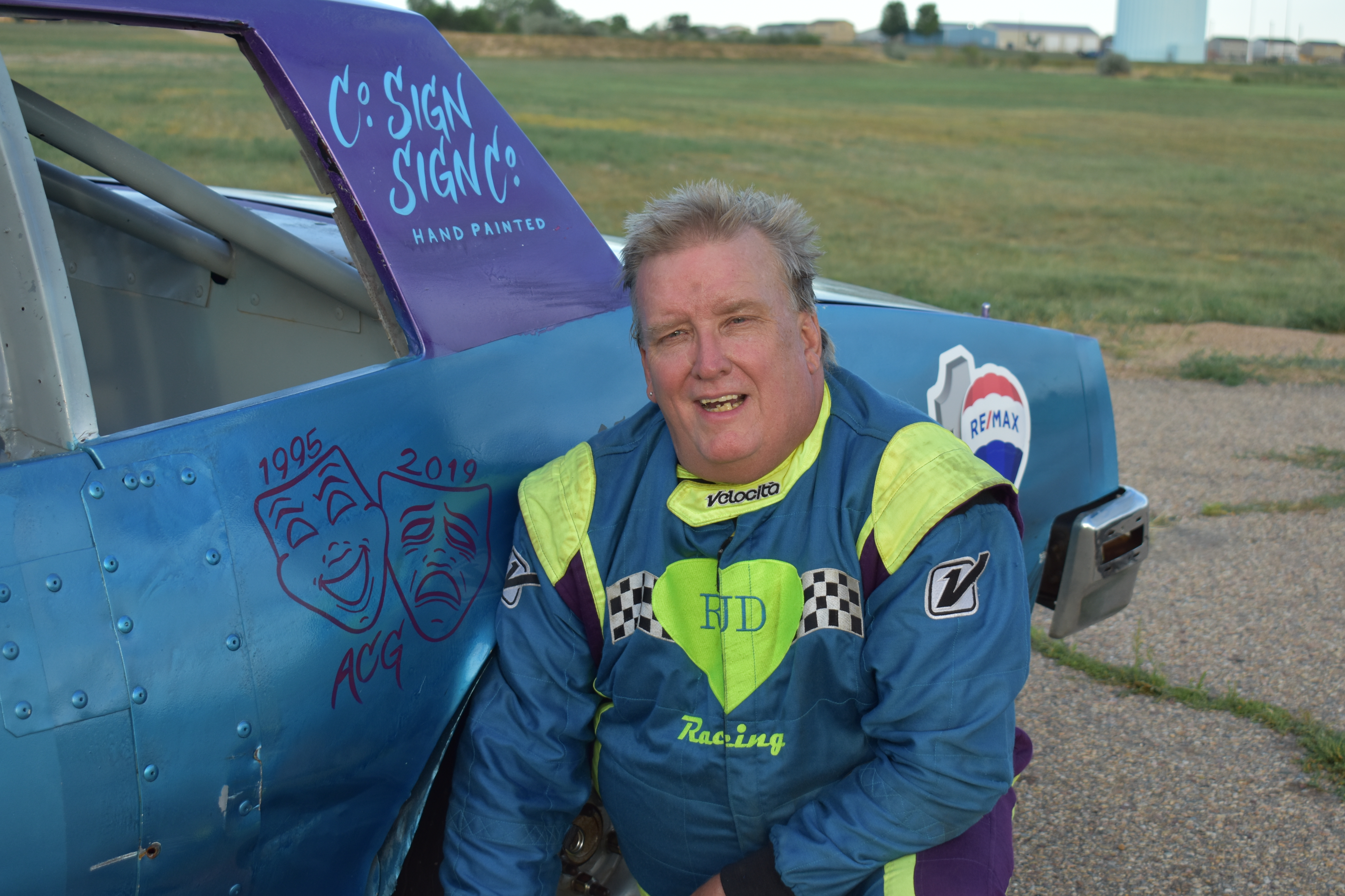 A race car driver kneeling next to his race car.