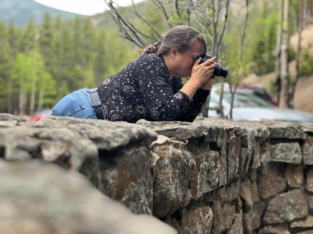A woman leaning over a brick wall taking a picture.